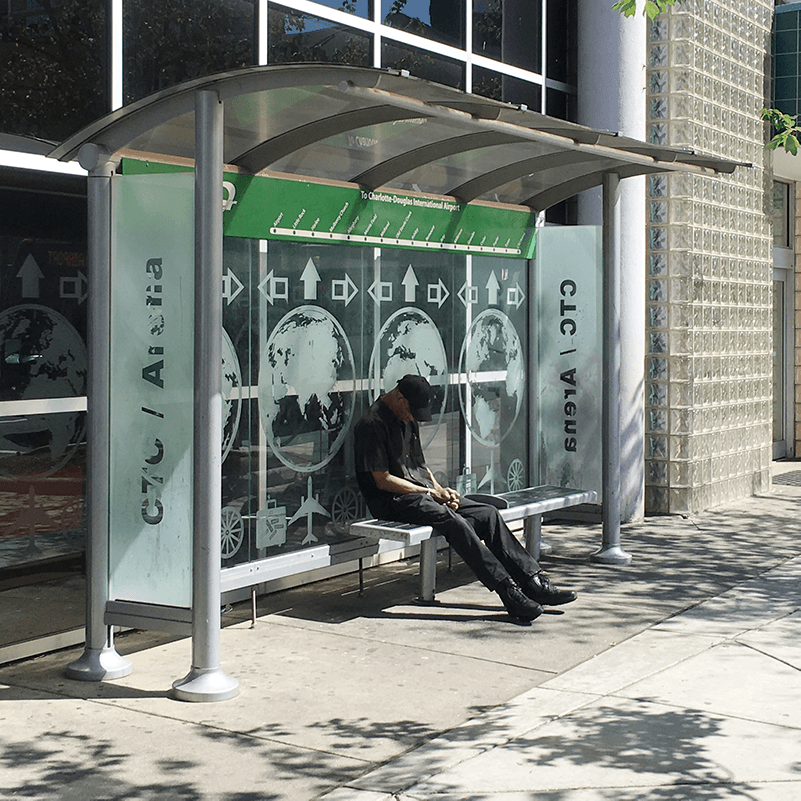 A man sits on a bench inside a bus shelter with a custom back wall design with an earth design.