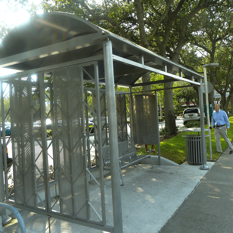 A bus shelter from the left side with bench seating inside and a trash receptacle on the outside right.