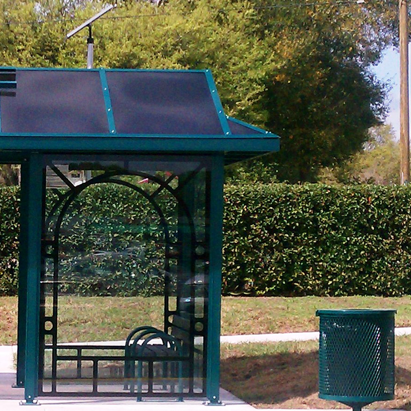 The right side of a bus shelter is seen with a trash receptacle on the outside right.