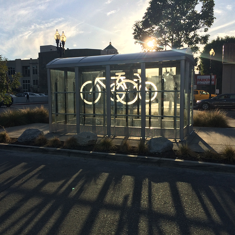 A bike shelter or locker is seen from the side with the sunlight shining through from the other side.