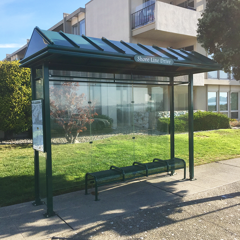 A sierrna bus shelter by Tolar with bench seating for four, rider information display on the left side panel and glass siding.