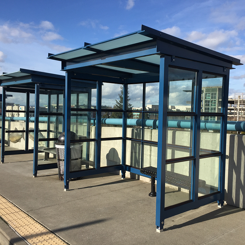 Two bus shelters are seen alongside a road with bench seating inside and a trash receptacle between the two.