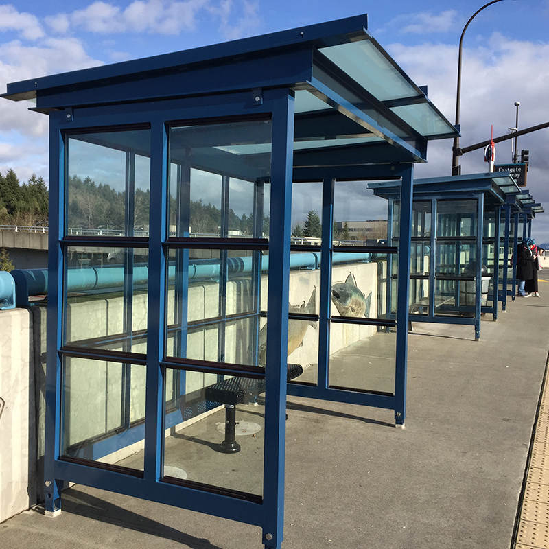 Multiple bus shelters are seen alongside the road with bench seating and standing room inside the shelter and trash receptacles between shelters.