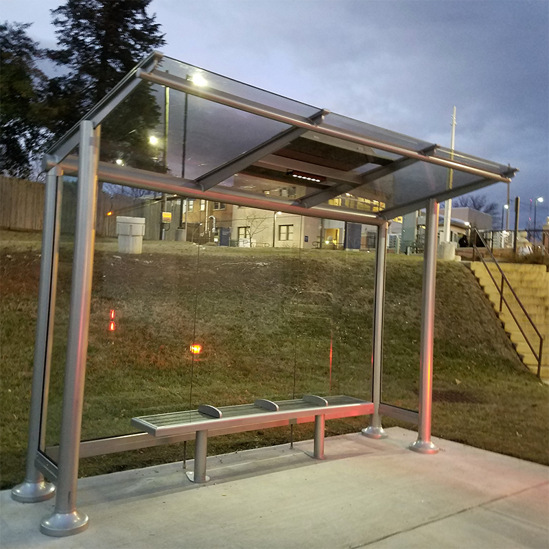 A signa bus shelter is seen at dusk with a bench for four and glass side panels.