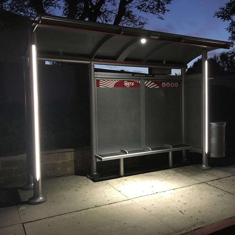 An MTS bus shelter seen at night with overhead lighting on and bench seating inside the shelter.