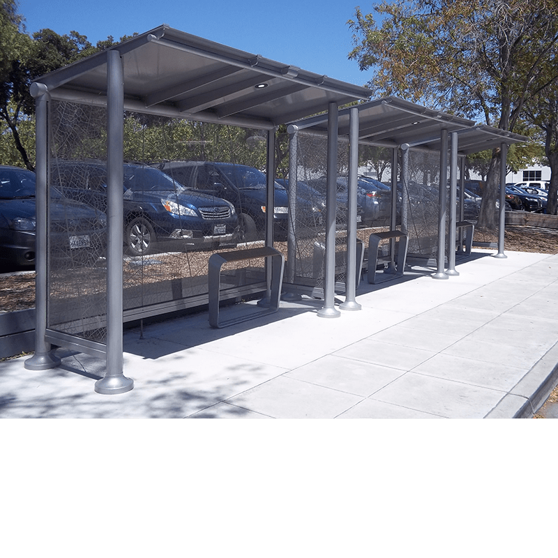 A bus shelter is seen in front of a parking lot with leaning seats under three separate shelters.