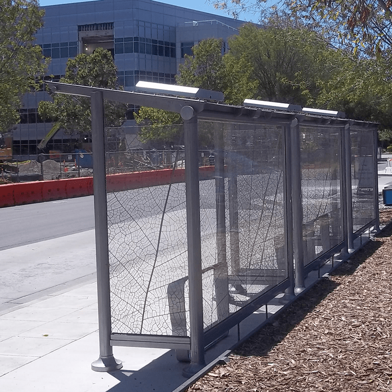 Bus shelters are seen from the back right with a leaf design on all the glass panels and leaning benches inside the three side by side shelters.