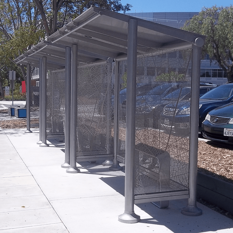 A bus shelter is seen from the right side with a leaf printed design on the glass side panels and leaning benches inside each shelter.