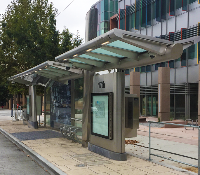 A bus shelter is seen from the right side with a right side digital display bench seating in the middle and another digital display on the left end.