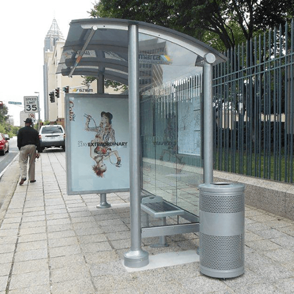 A bus shelter seen from the right side with a trash receptacle on the outside right, bench seating inside and a left side panel for advertising.