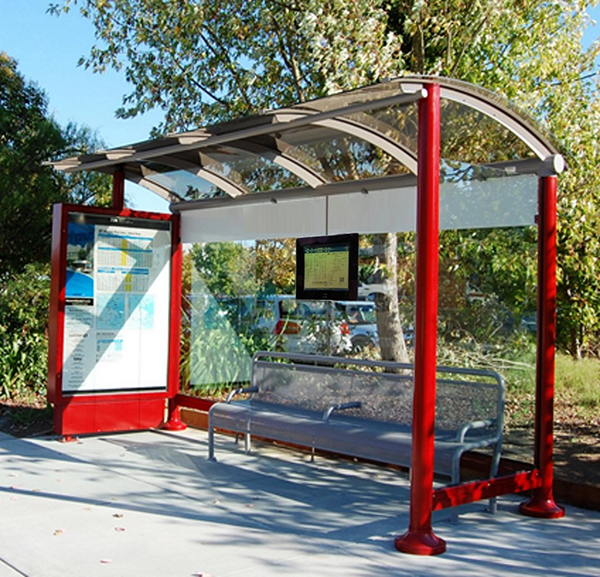 A bus shelter seen from the front right with a left side panel for advertising, bench seating and a digital display for rider information on the center back panel.
