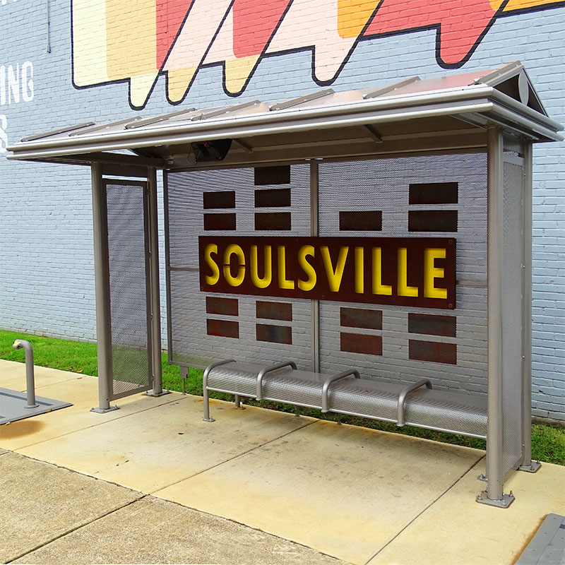 A custom bus shelter is seen from the front right with bench seating and a custom back to the structure reading Soulsville.
