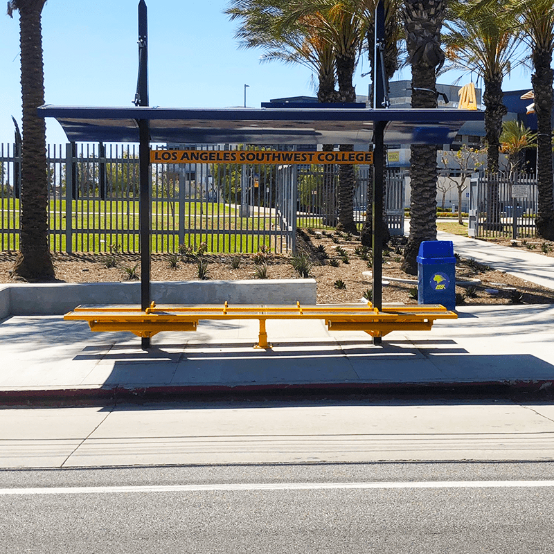 A bus shelter outside of Los Angeles Southwest College with double sided benches and an arched roof for ample coverage for riders.