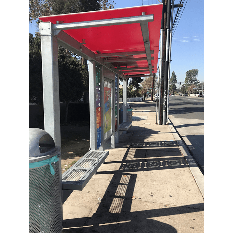 Side view of a red roof, metal bus shelter with trash receptacle, seating and advertising displays