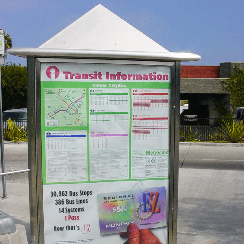 A three sided rider information kiosk with metro information, maps and an advertisement at the bottom.