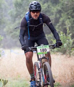 Tolar employee Carlos Garcia seen riding his bike through nature with a water backpack and helmet on