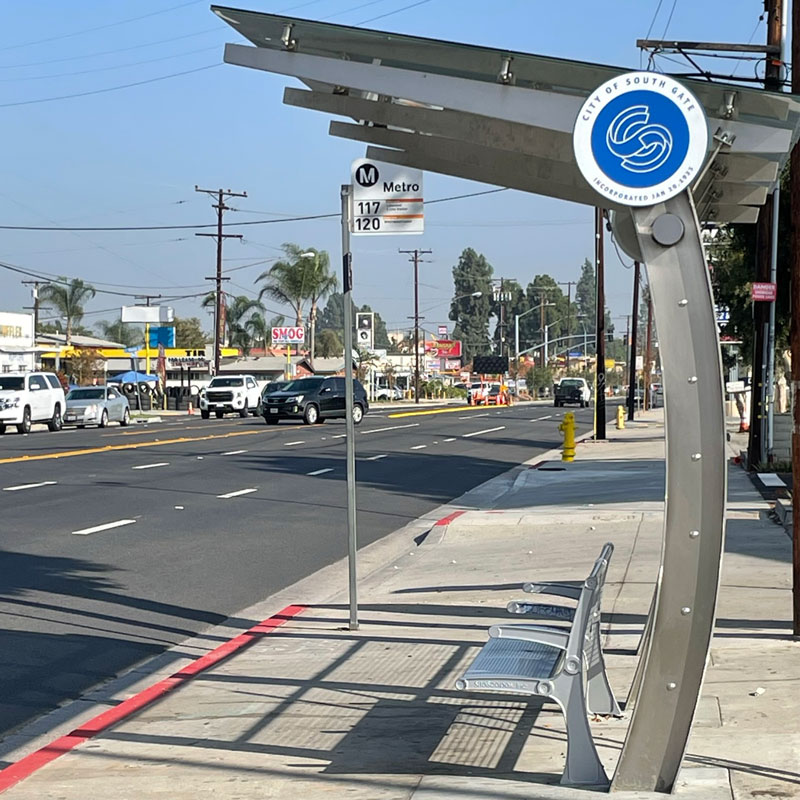 A bus shelter is seen from the left side in South Gate with a curved structure and bench seating.