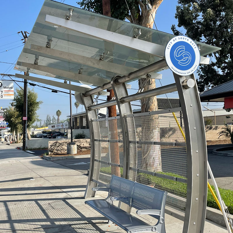 A signa custom bus shelter is seen from the front right side with an arched structure and bench seating for two in South Gate.