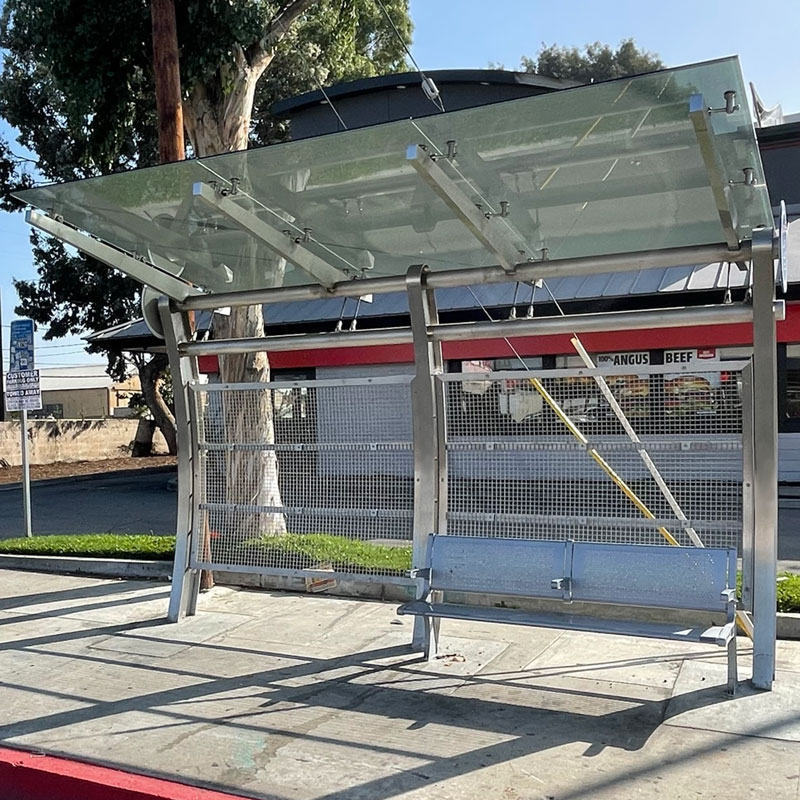A signa custom bus shelter is seen from the front with an arched structure design and a large bench for rider seating.