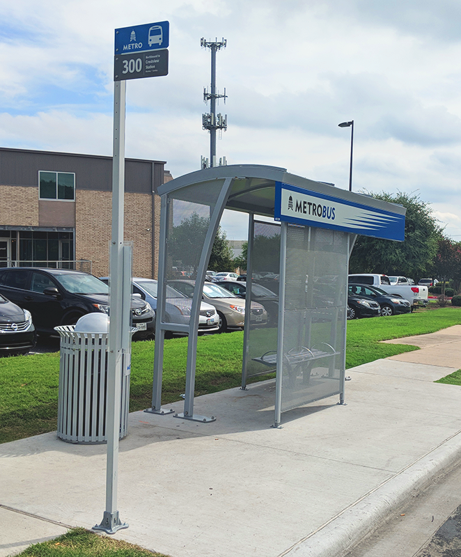 A MetroBus bus shelter is seen from the front left side with a trash receptacle on the left and a bench inside the shelter on the right.
