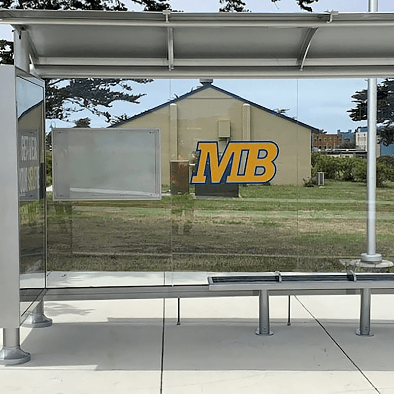 A siga sunset bus shelter with glass siding, a rider information display on the back panel, a custom MB logo on the back and bench seating for three.