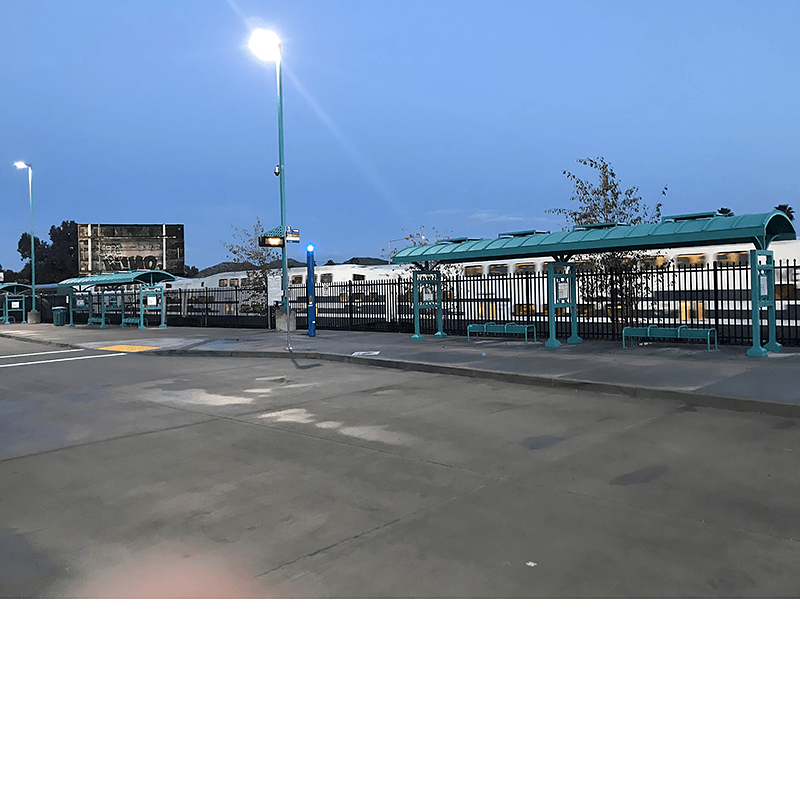 A transportation hub is seen with bus shelters with bench seating in front of a train passing by the station.