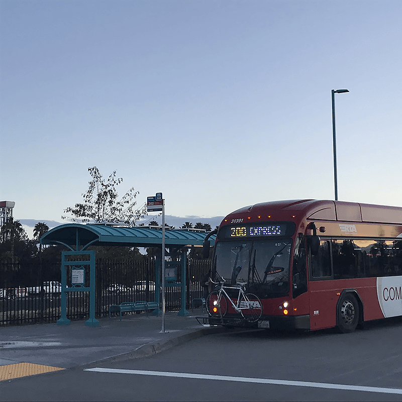 A bus arrives at a bus shelter with rider information displayed on the shelter itself and on the post near the street.