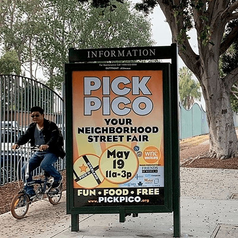 A man rides by an information kiosk with an advertisement showing.