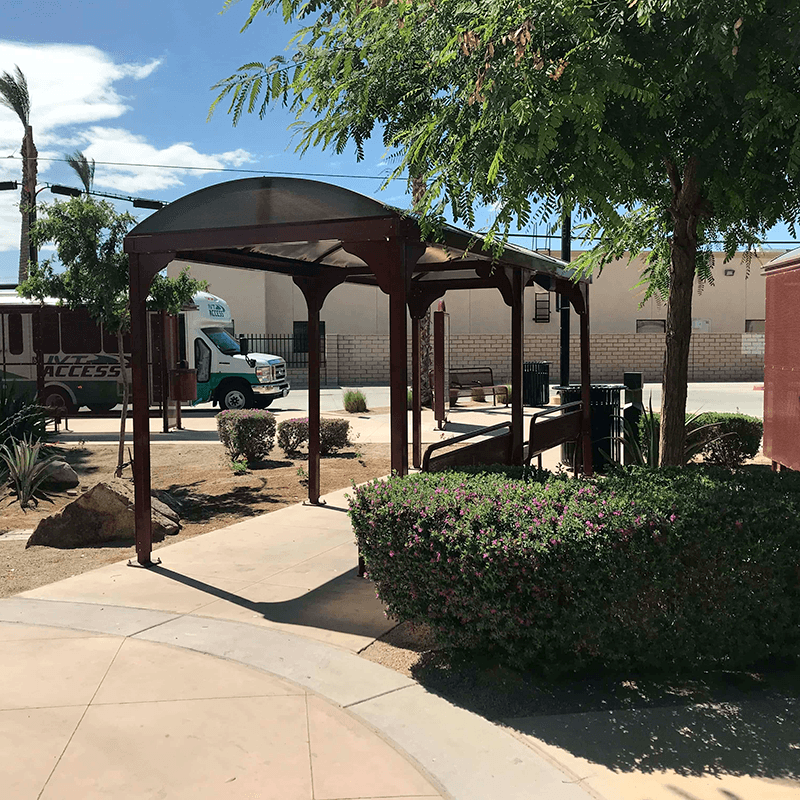 A bus shelter seen from the back right with two benches and a trash receptacle on the outside of the shelter.