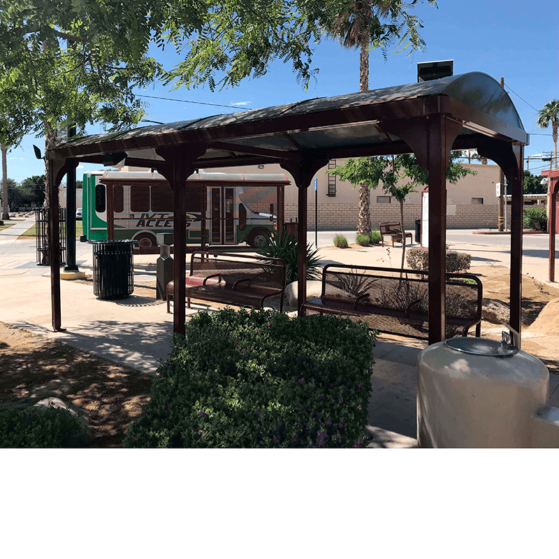 A bus shelter with two benches and a trash receptacle and water foundation on the outside.