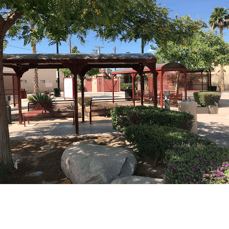 Multiple bus shelters are seen in a landscaped area with bench seating, water foundations and trash receptacles.