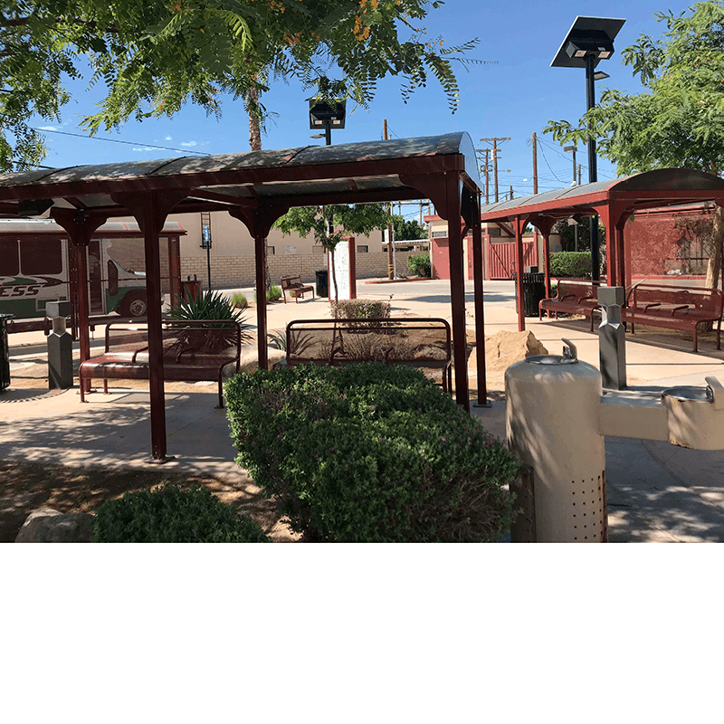 Multiple bus shelters are seen scattered throughout a landscaped area with benches under the shelters and water foundations and trash receptacles placed on the outside.