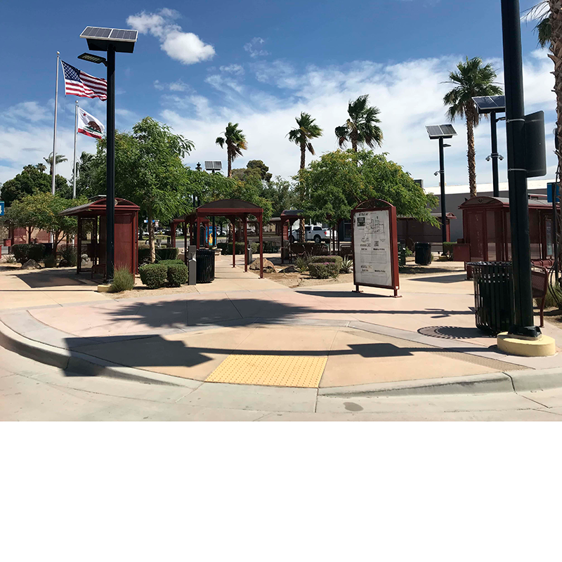 Multiple bus shelters are seen scattered throughout a landscaped area with benches under the shelters and water foundations and trash receptacles placed on the outside and a rider information display placed at the front.