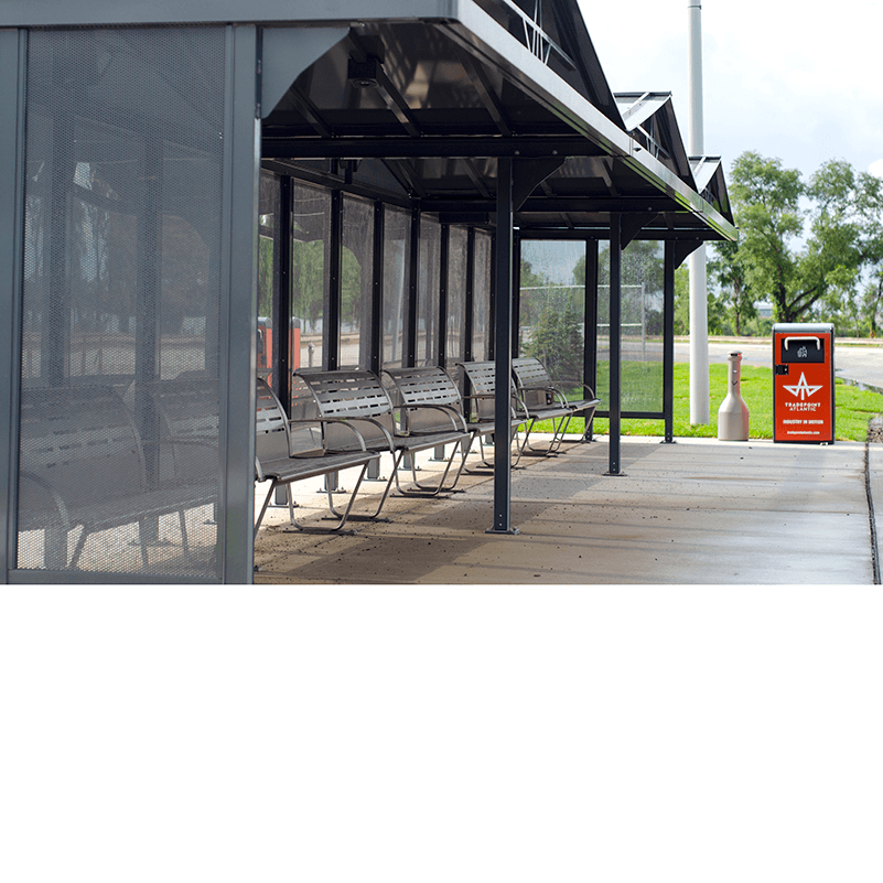 A bus shelter seen from the front left side with six benches inside the shelter and trash and cigarette receptacles on the outside right of the shelter.