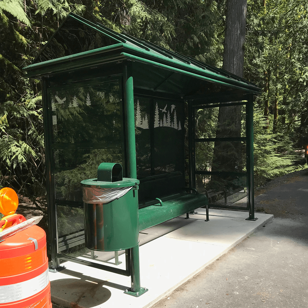 A bus shelter with bench seating, a rider information display on the left side panel and a trash receptacle attached on the left outside.
