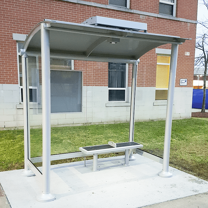 A bus shelter with bench seating for two, glass panel siding and a solar panel on top for the light inside the shelter.
