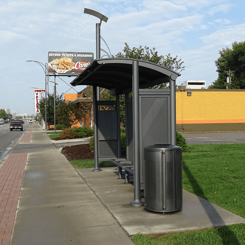 A signa bus shelter seen from the front right with a trash receptacle on the right, bench seating inside and a rider information display on the left side panel alongside a busy street.