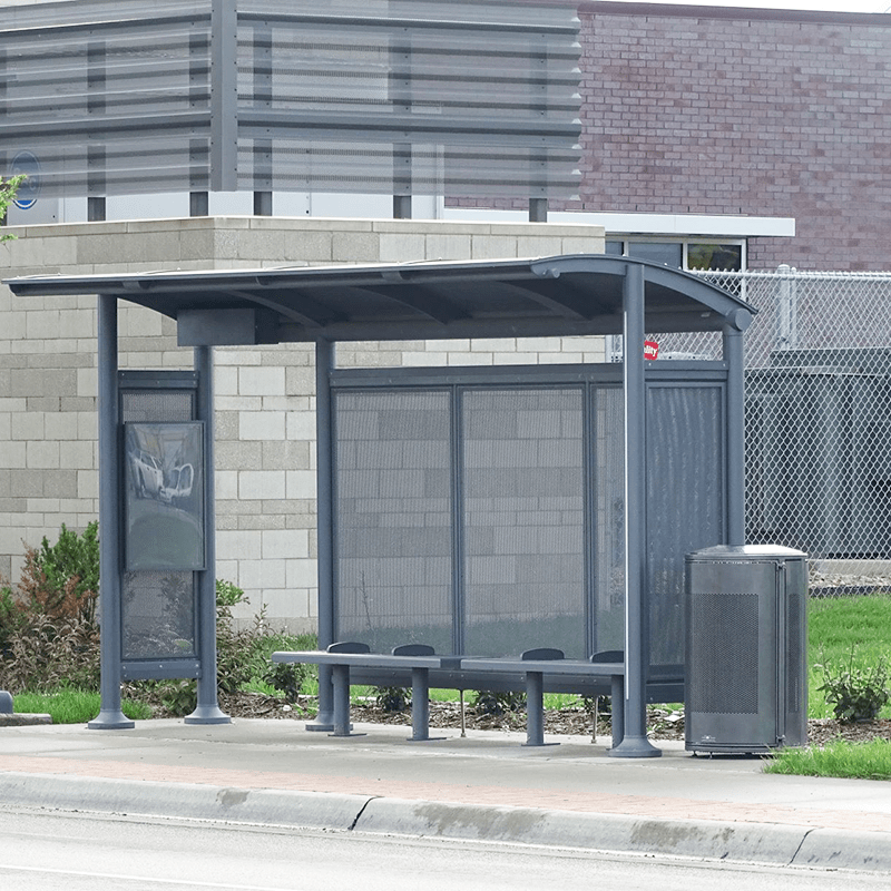 A bus shelter seen from the street with a trash receptacle on the right side, bench seating in the shelter and a left panel rider information display.