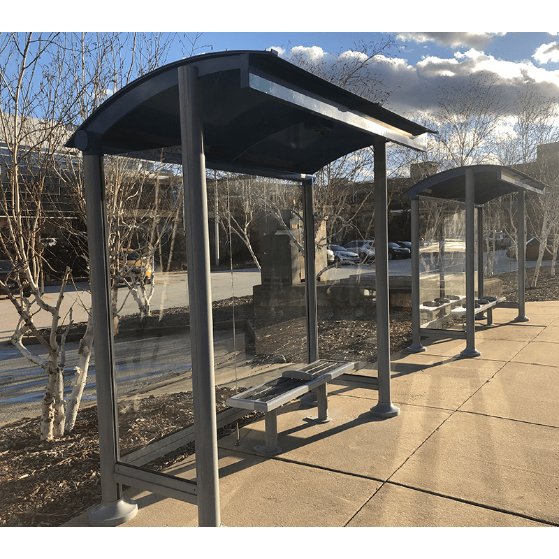 Two bus shelters are seen from the front left side with glass siding and bench seating.