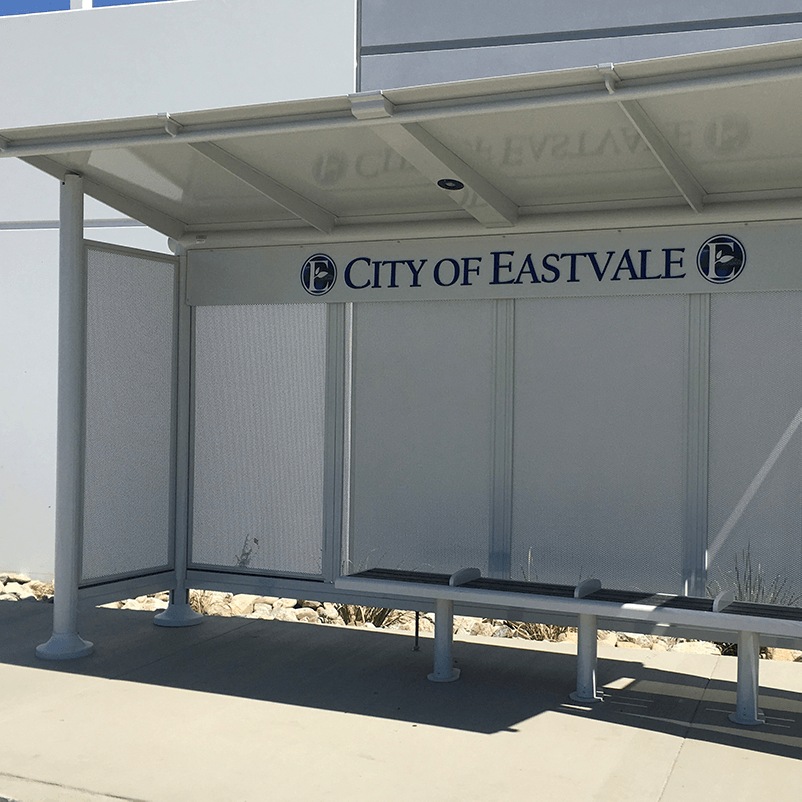 A bus shelter with a custom back panel sign reading City of Eastvale with bench seating below.