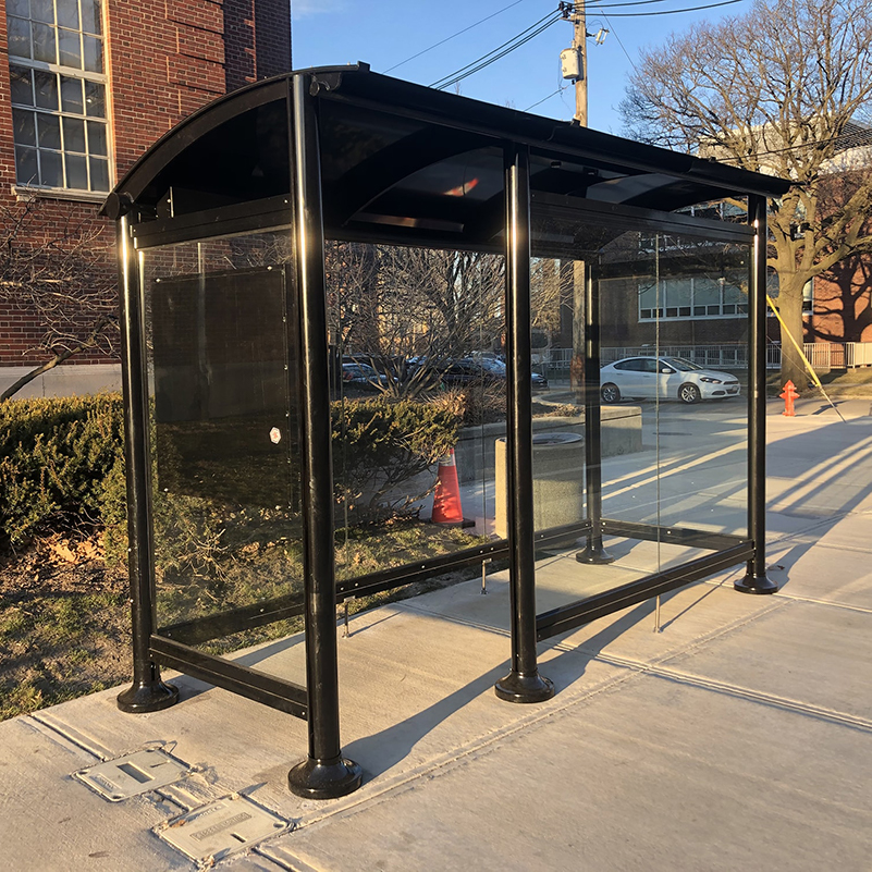 A signa sunset bus shelter is glass siding and rider information display with a one panel wide opening to shelter riders from the elements.