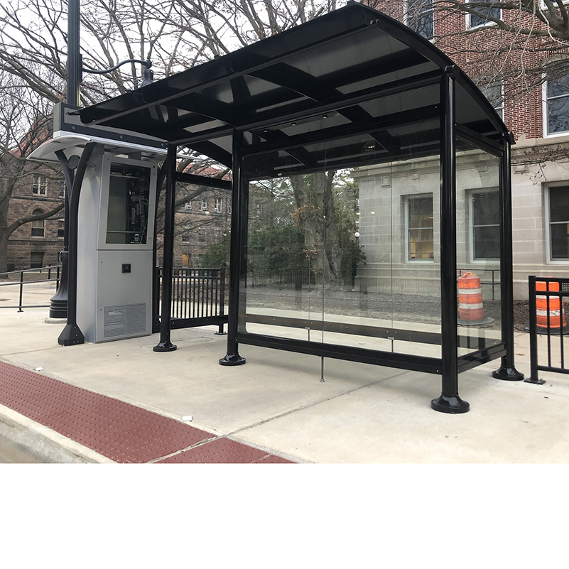 A signa sunset bus shelter is glass siding and rider information display with a one panel wide opening to shelter riders from the elements.