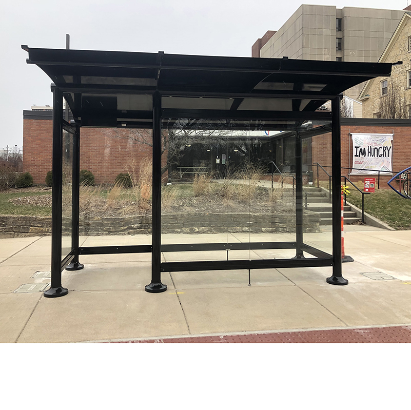A signa sunset bus shelter is glass siding with a one panel wide opening to shelter riders from the elements.