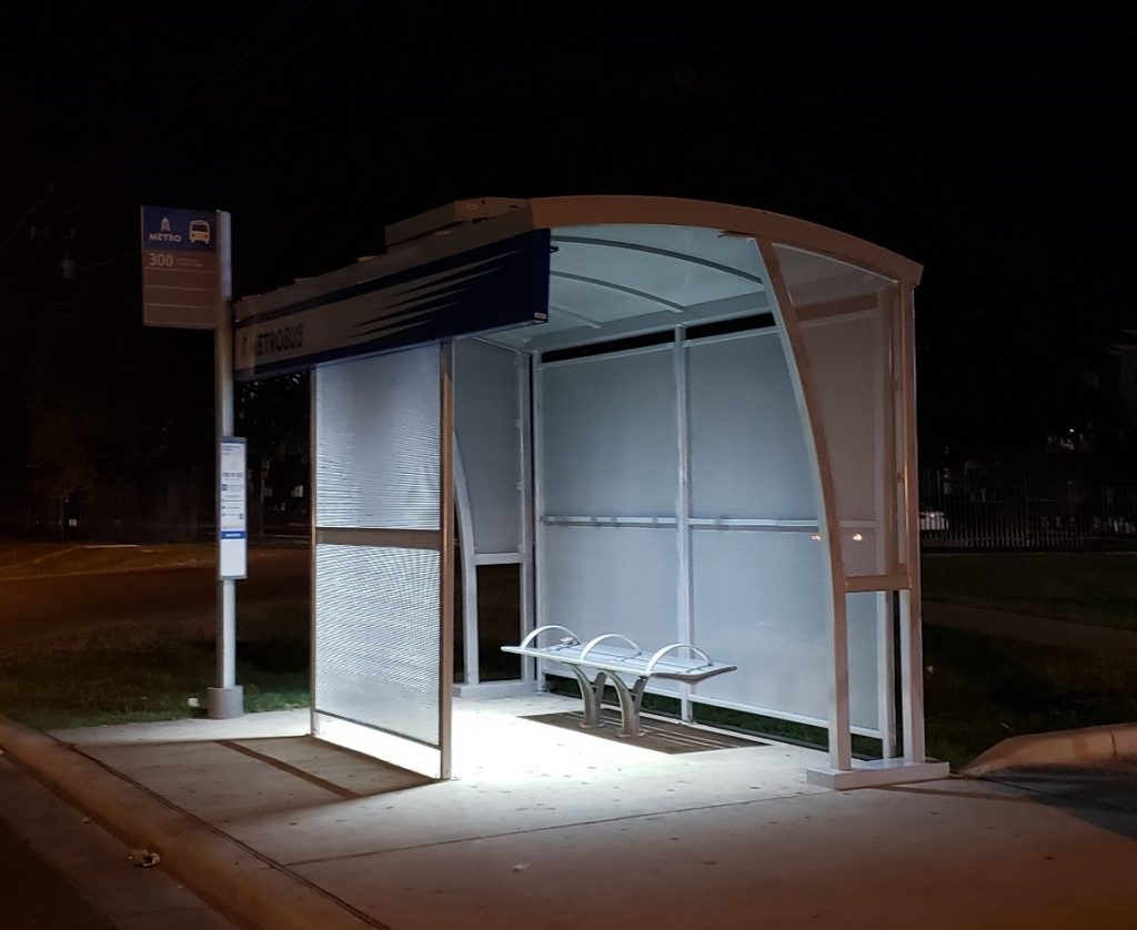 A metro bus shelter from the left side at night with bench seating and lighting