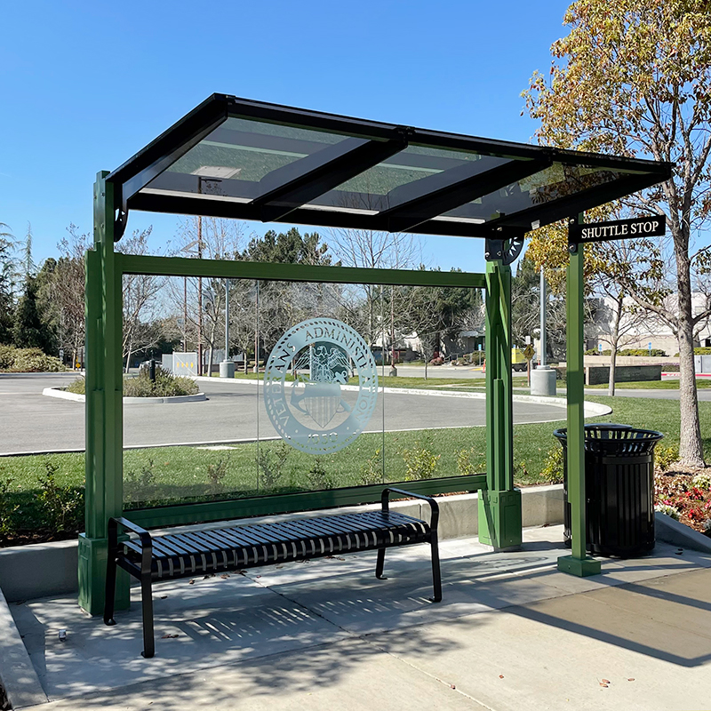 A signa custom bus shelter with a back glass panel with custom logo, bench seating under the shelter and a trash receptacle on the outside right.