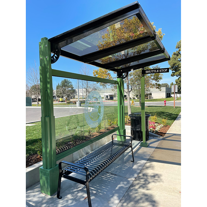 A signa custom bus shelter with a back glass panel with custom logo, bench seating under the shelter and a trash receptacle on the outside right.