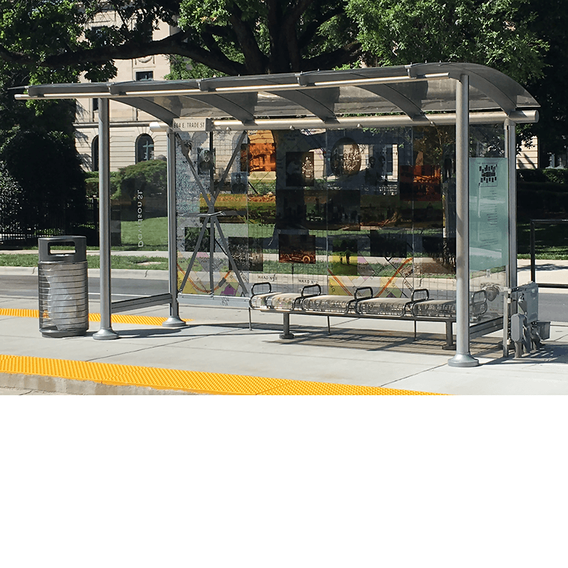 slight left side view of a bus shelter designed with bench seating, a trash can nearby and rider information displayed inside