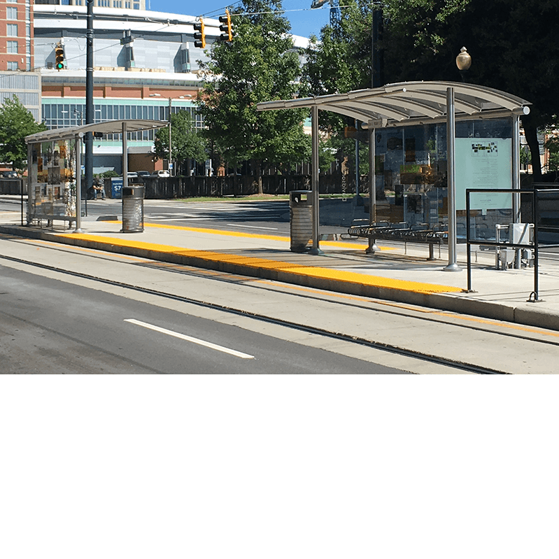 Side view of two bus shelters, one facing to the left and one facing the street to the right. Both have a custom design back wall with images and bench seating for riders