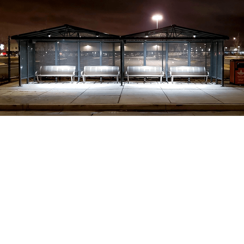 Two bus shelters sit side by side at night with overhead lighting for the two benches situated under each shelter.