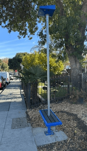 A bus stop sign is seen from the right side with seating on either side of the post and a light on top.